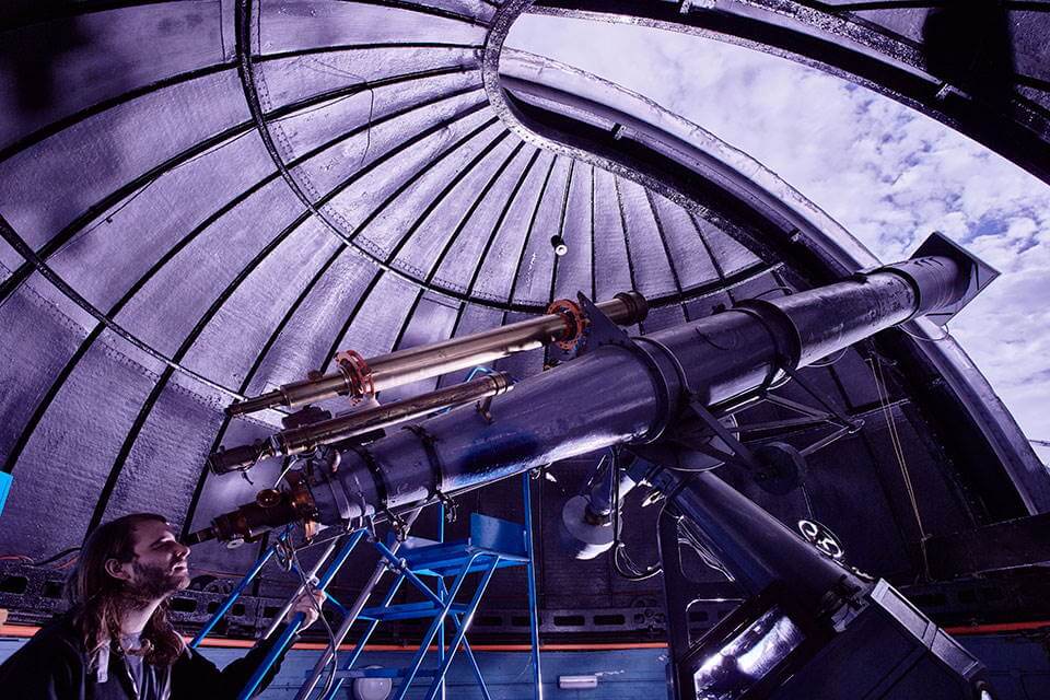 large telescope pointing up to the sky through an observatory dome, a person looking up into it.